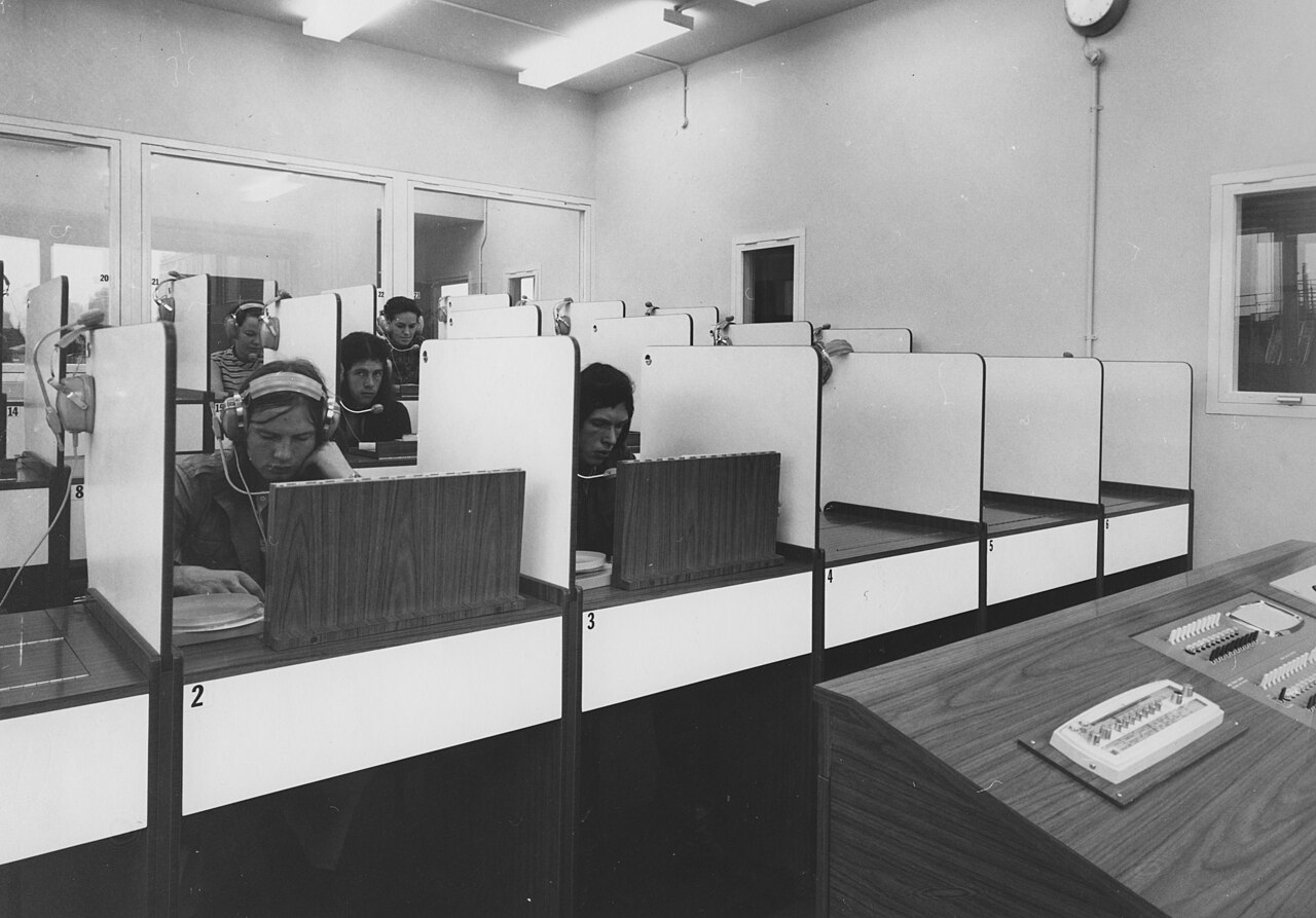 Black-and-white photograph of language students wearing headsets in individual audio booths